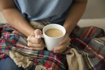 a woman with a plaid blanket in her lap holding a mug of coffee 