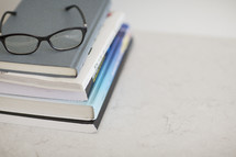 A pair of black eyeglasses on top of a stack of books.