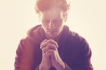 a man with praying hands under glowing light 