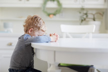 toddler boy praying at a kitchen table 