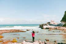 a girl standing on a shore looking into a tide pool 