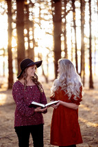 two women reading a Bible outdoors in the woods in autumn 