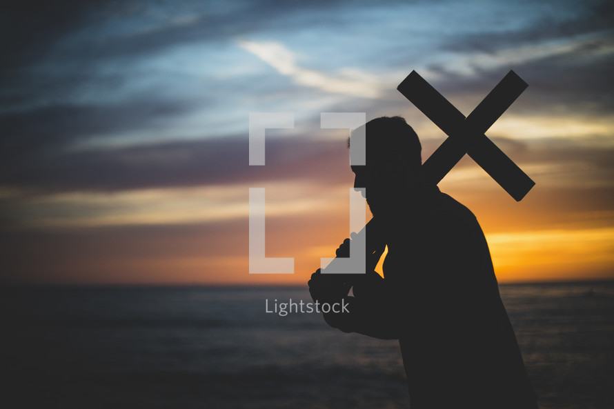 silhouette of a man holding up a cross at sunset 