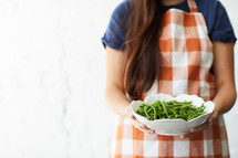 a woman holding a bowl of green beans 