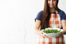 a woman holding a bowl of green beans 