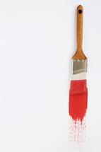 A paint brush with red paint on a white background.