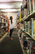 woman standing in a library looking at books on a bookshelf 