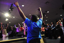 Congregation around center stage with arms raised praising God during worship service.