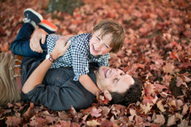 a father and son playing in fall leaves 