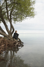 a man sitting on tree roots looking out at water