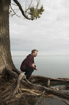 a man sitting on a tree roots looking out at the ocean 