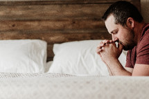 a man kneeling in prayer over a bed 