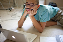 boy resting a pencil under his nose while he works on a computer