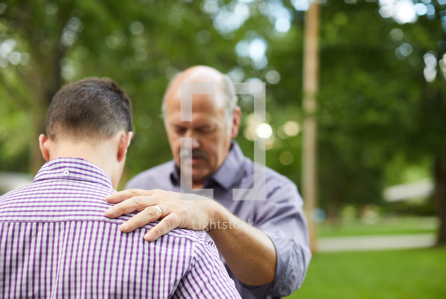 mentor praying over another man outdoors 