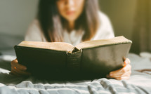a woman reading a Bible in bed 