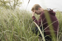 a man squatting in tall grasses and praying deeply