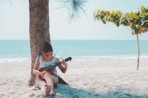woman sitting on a beach playing a ukulele 