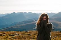 a woman in a sweater standing on a mountaintop 