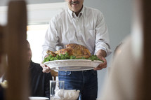 a man presenting the turkey to the table at Thanksgiving 