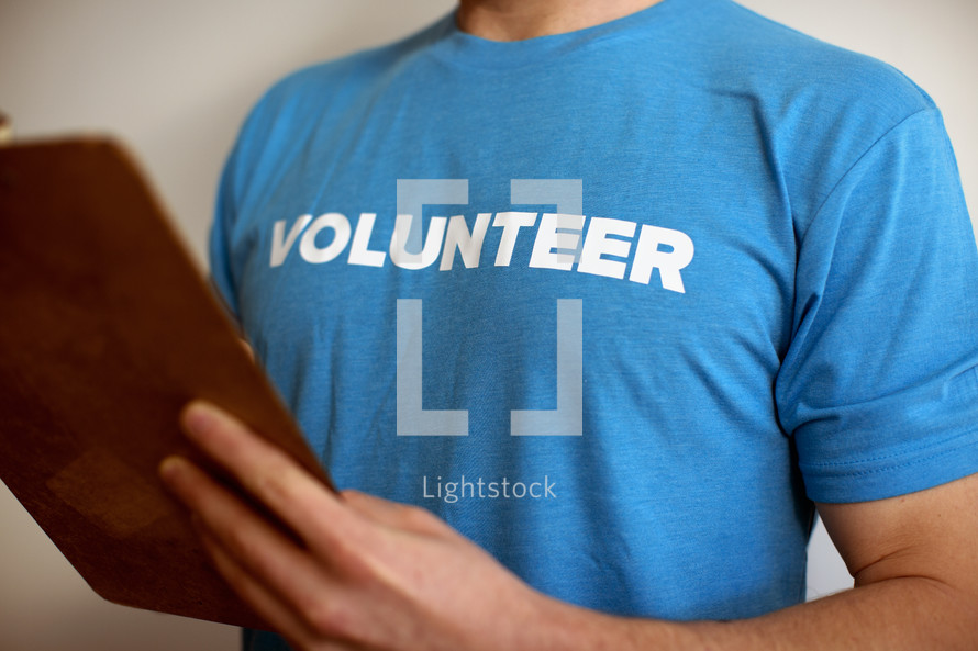 A man in a volunteer t-shirt holding a clipboard.