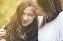 a mother kissing her teen daughter on the cheek 