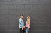 a couple walking holding hands in front of a gray wall 