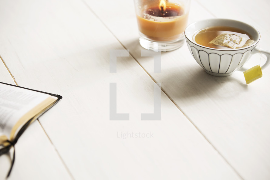 tea, Bible, and candle on a white wood table. 