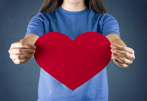 A teenage girl holding out a red heart.  Plenty of space to add your own text.