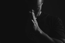 a man with praying hands in dramatic lighting.
