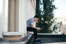 a man sitting on a rooftop texting on his cellphone 