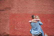 a couple hugging in front of a red brick wall 