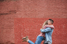 a couple hugging in front of a red brick wall 