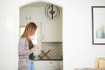 a woman standing in a kitchen with a mug 