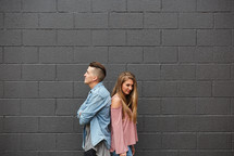 a couple standing back to back in front of a gray wall 