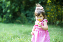 a toddler girl smelling a flower 