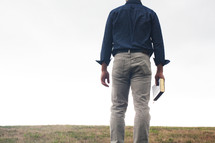 a man standing in a field holding a Bible 