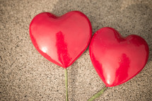 Two red hearts on sticks laying on a textured background
