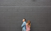 a couple standing back to back in front of a gray wall 