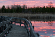 A wooden pier across a pond at sunset.