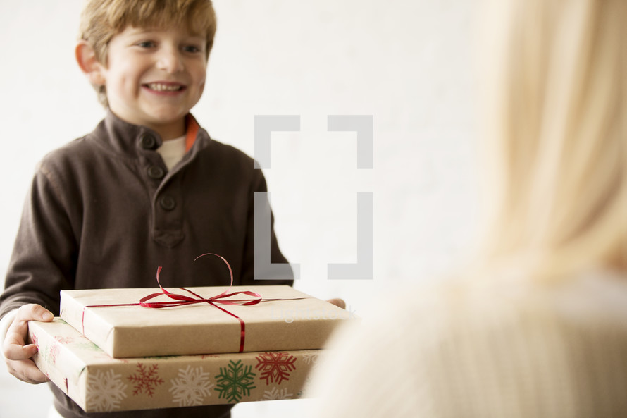 a young boy handing a Christmas gift to his mother 