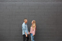 a couple standing in front of a gray wall holding hands 