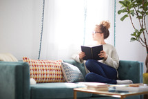 a woman reading a book sitting on a couch 