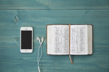 iphone 6 and earbuds and open Bible on a teal table 