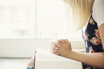 woman sitting on a couch with a Bible in her lap and praying hands.