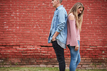 a couple standing back to back in front of a red brick wall 