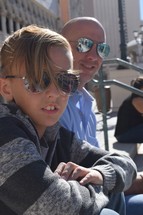 father and preteen son in Ray-Bans sitting on steps 