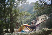 a woman in a hammock next to a tent in a campsite 