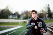 a young man in a letter-jacket holding a football 