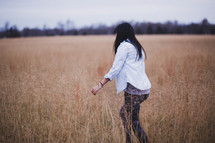 a woman walking through a field of tall grass 