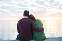 a couple hugging sitting on a pier at sunset 